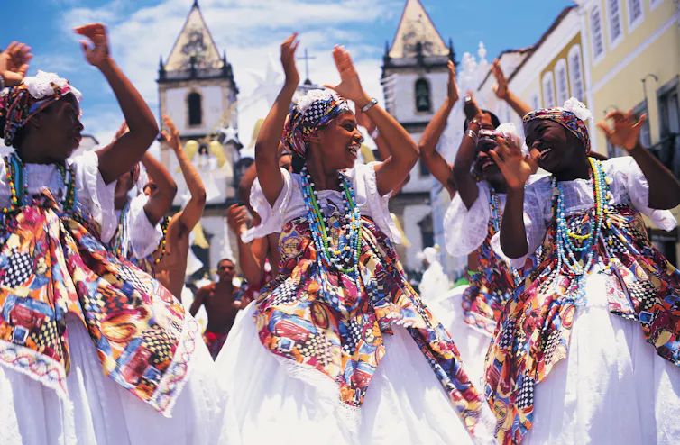 Los bailarines vestidos de blanco con alas de colores brillantes aplauden y ríen.