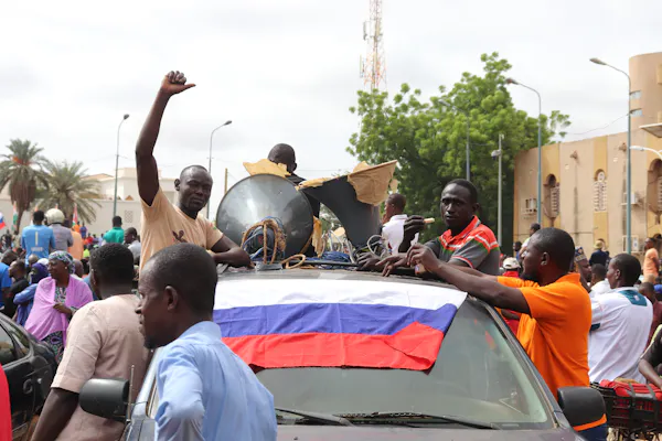 People in a car hold their fists aloft, while carrying a red, blue and white flag.