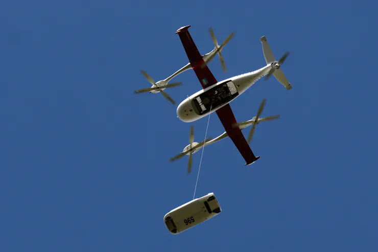 a small aircraft in the sky with an object suspended below it from a cable