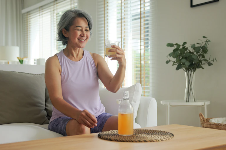 Woman smiling while looking at glass of kombucha she's holding