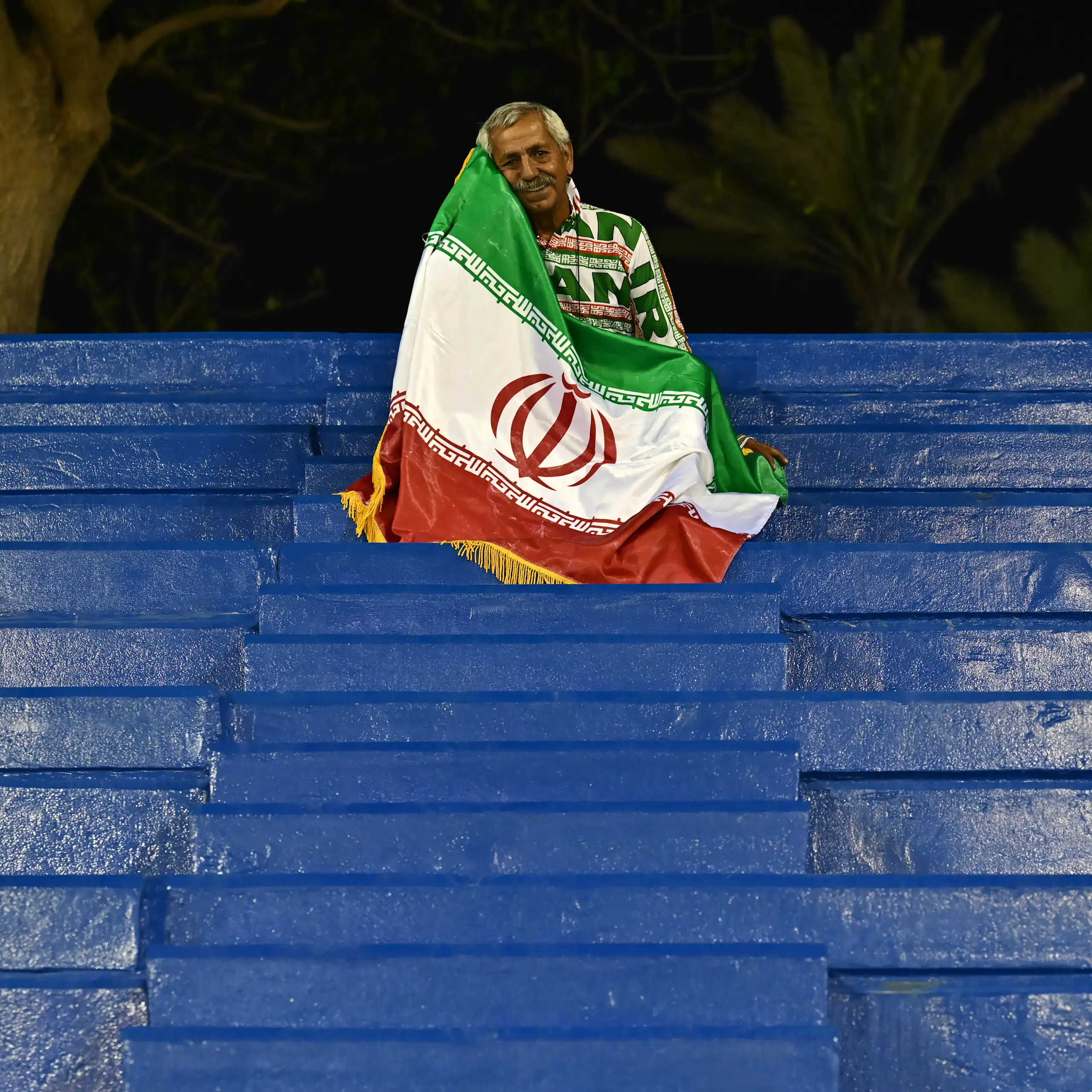 A man sits on seating draped in a flag.