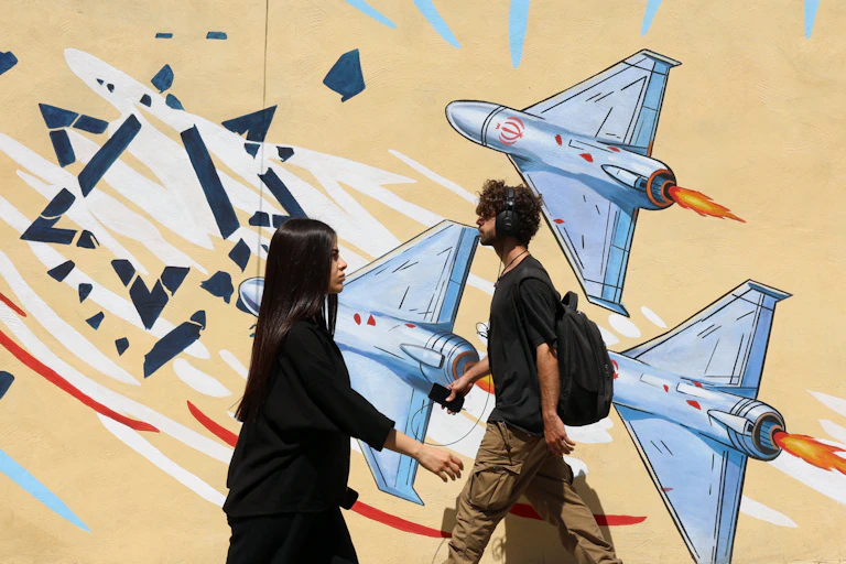 Two young people cross paths in front of a wall-painted mural showing war planes.
