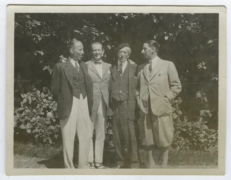 An old photo with four men standing in a garden.