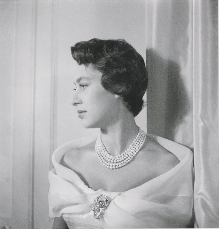 An old photo of a women in a fancy dress, pearl necklack and rose brooch, looking sidewats.