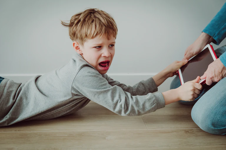 Little boy clinging on to tablet parent is taking away