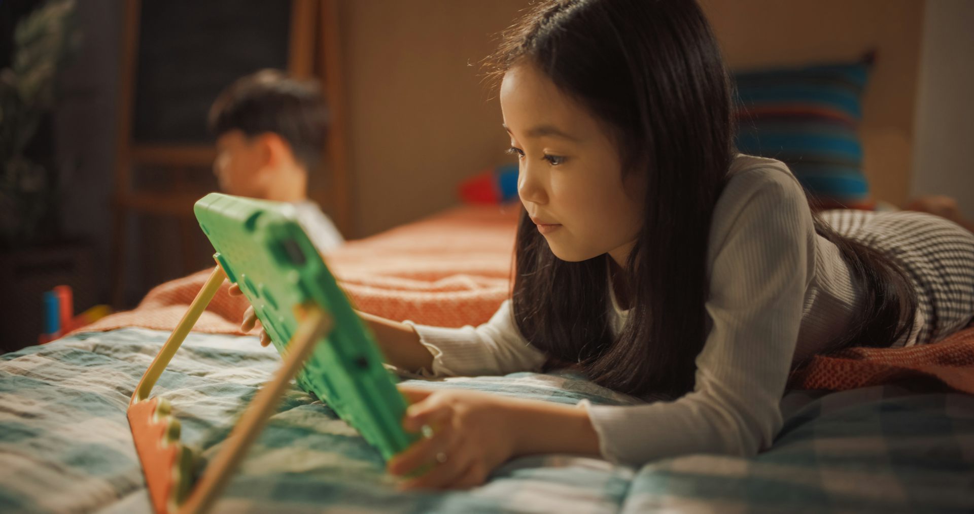 Girl lying on bed playing on tablet