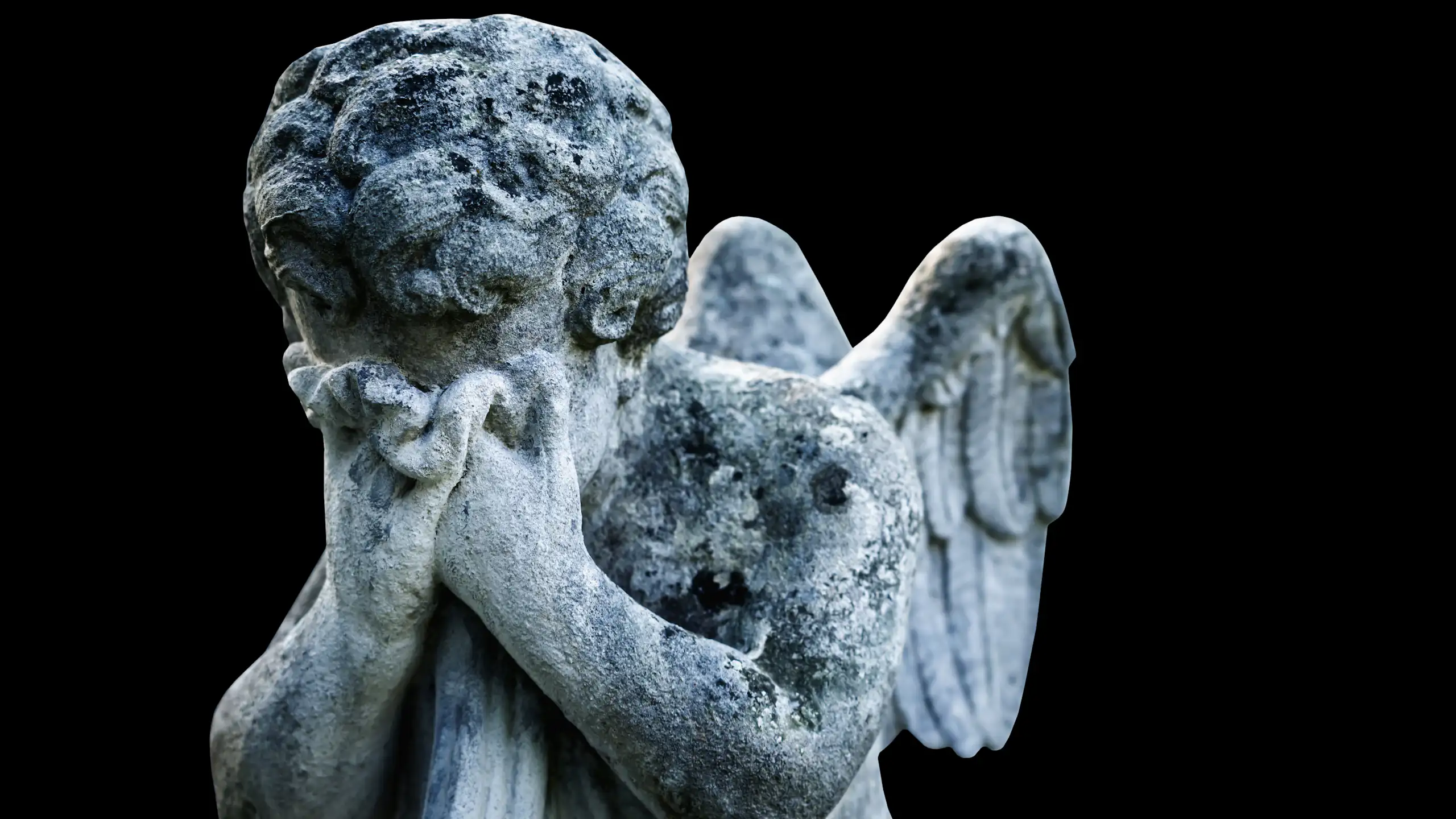 Sad angel as a symbol of pain and death. Ancient statue isolated on a black background