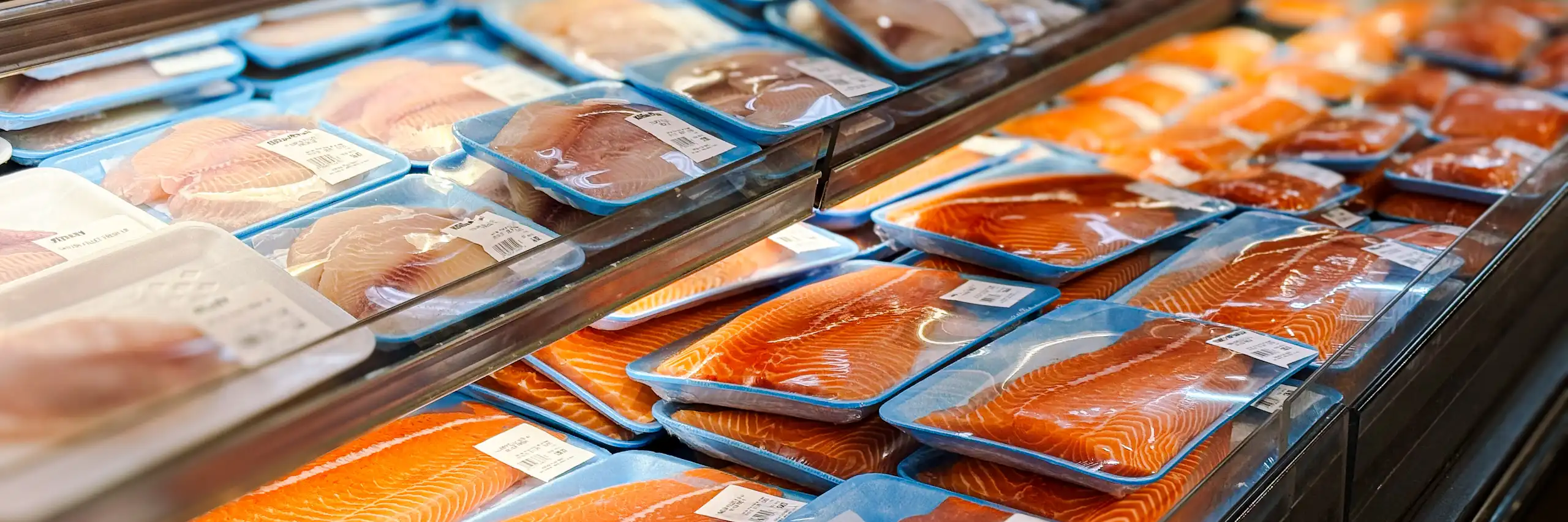 Des filets de saumon, tilapia et autres poissons conditionnés dans des barquettes bleues recouvertes d’un film plastique, au rayon frais d’un supermarché.