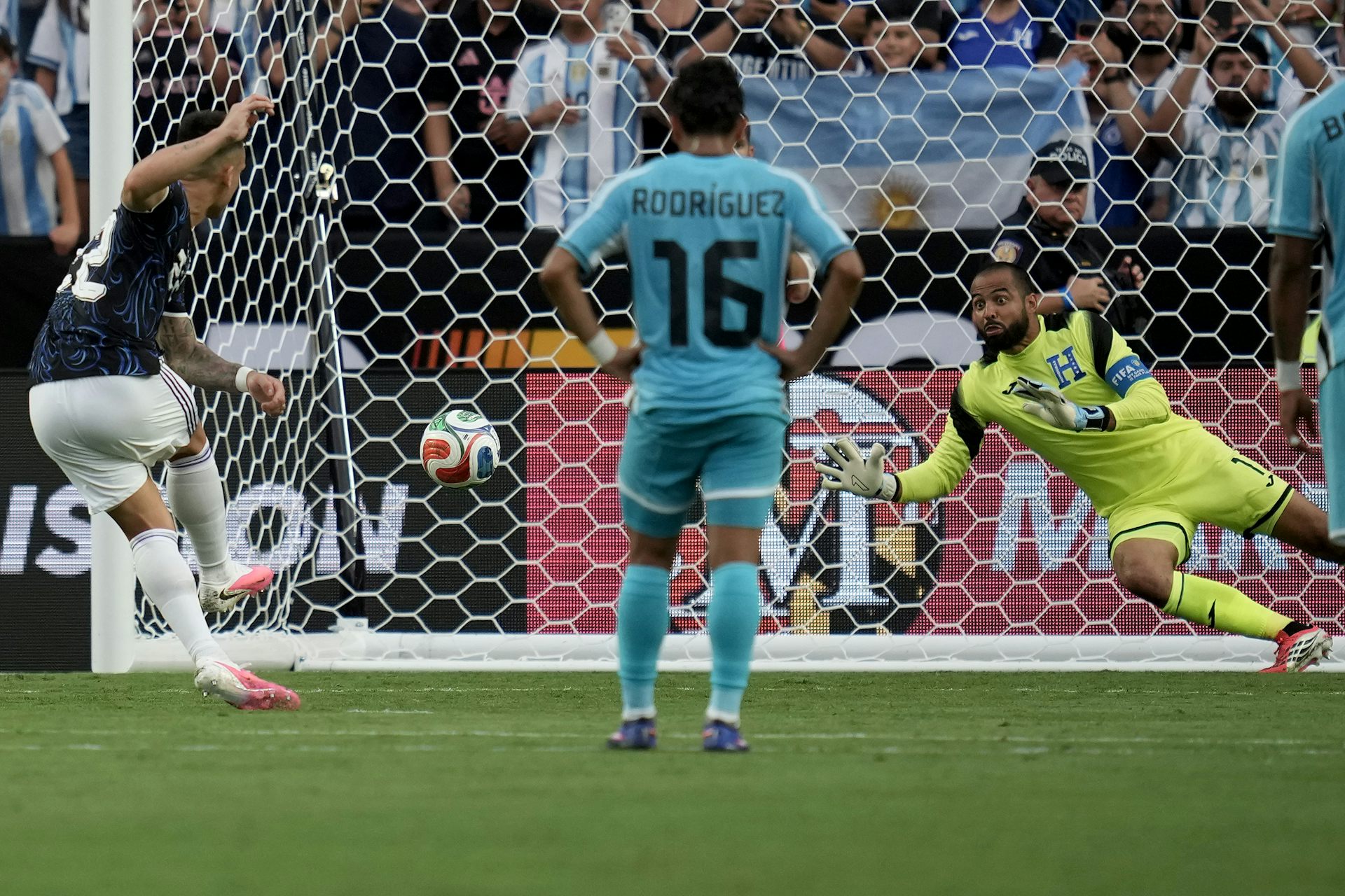 El futbolista se sitúa de cara a la red mientras el portero salta a por el balón.
