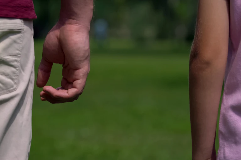Close-up of man's arm with a space between his daughter's arm, suggesting distance and coldness.