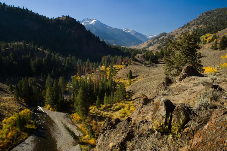 A landscape view across the East Fork of the Salmon River with colorful valleys and snow-capped mountains in the distance.