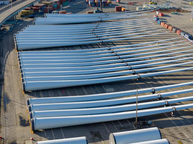 Several long white poles sit in a row on an area of pavement.