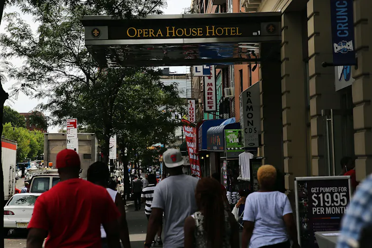 El brote de enfermedad del legionario en Filadelfia en 1976 fue misterioso y mortal; 50 años después, los científicos conocen la causa, pero los brotes continúan 3 La gente camina por la calle cerca del edificio que dice Hotel Opera.