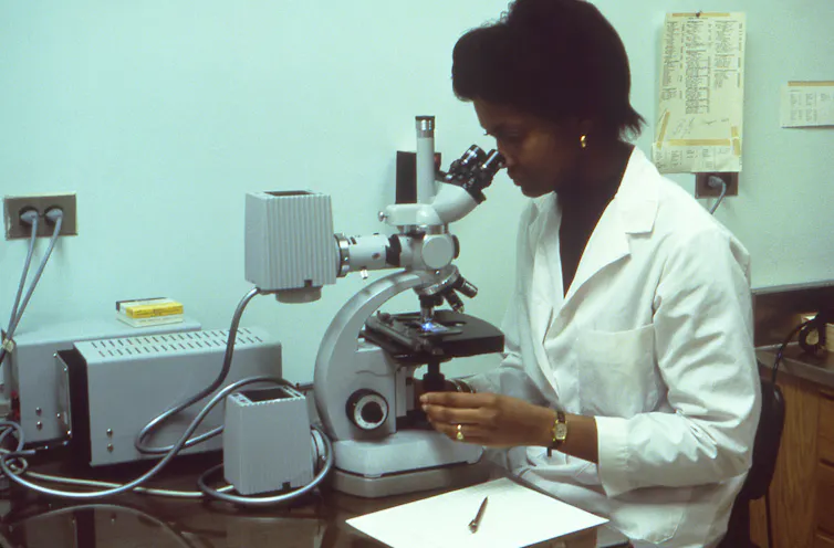 El brote de enfermedad del legionario en Filadelfia en 1976 fue misterioso y mortal; 50 años después, los científicos conocen la causa, pero los brotes continúan 1 Una mujer con una bata de laboratorio blanca mira a través de un microscopio.