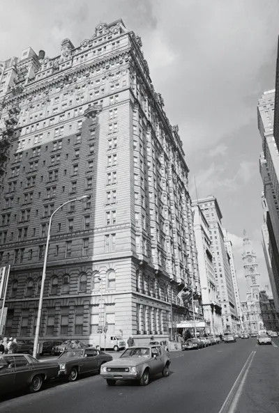 Black-and-white photo of large ornate building alongside two-way street with 1970s-era cars