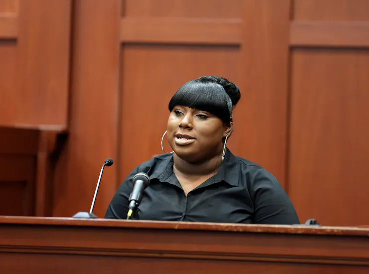 A young woman testifying on a witness stand, sitting near a microphone