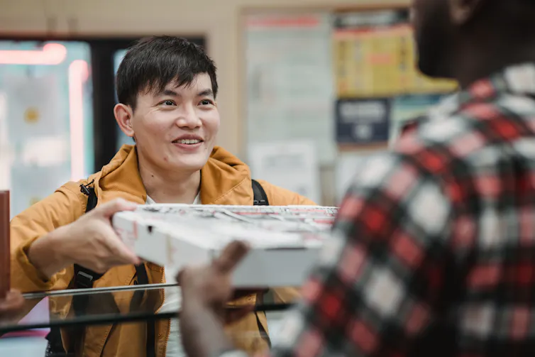 Pizza shop worker hands a pizza over to another man