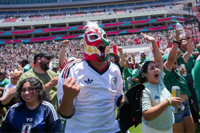 Soccer fans cheer loudly for their team, with the central fan wearing a red, green and gold mask.