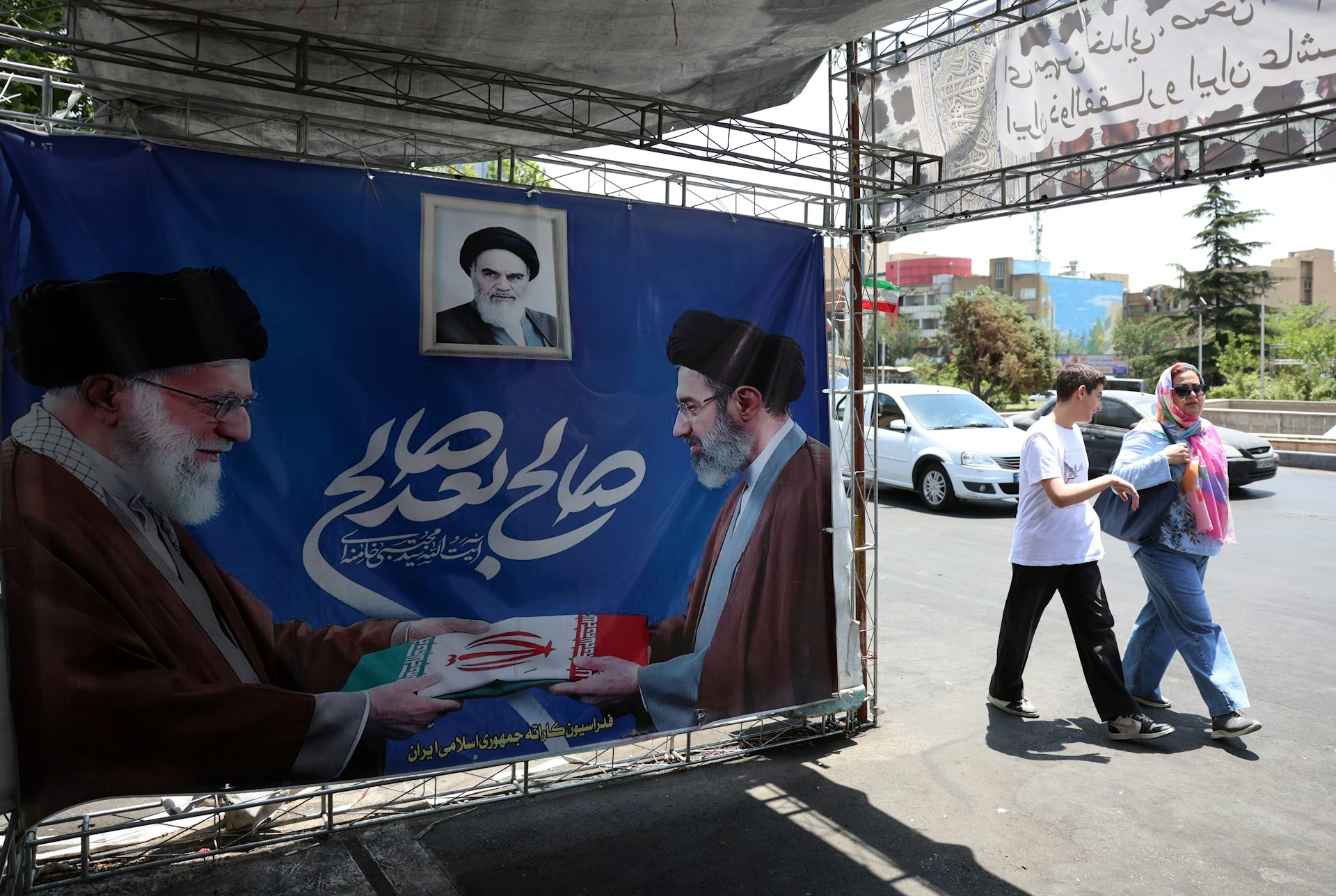 Iranians walk past a poster featuring the late Iranian supreme leader, Ayatollah Ali Khamenei, alongside his son and successor, Ayatollah Mojtaba Khamenei.