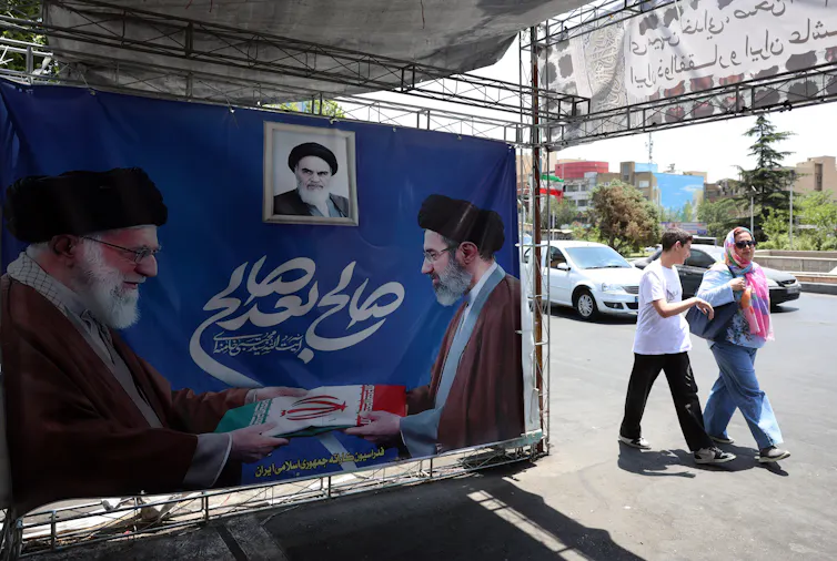 Iranians walk past a poster featuring the late Iranian supreme leader, Ayatollah Ali Khamenei, alongside his son and successor, Ayatollah Mojtaba Khamenei.