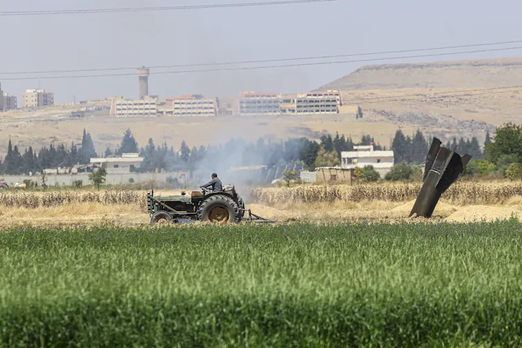 A man drives a tractor near the remains of an Iranian missile that landed in a field in Syria.