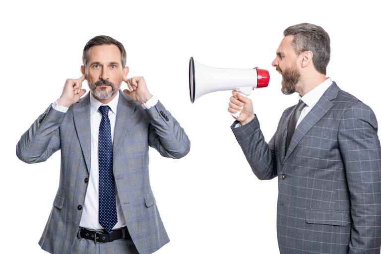 Homme parlant avec un mégaphone dans l'oreille d'un autre homme qui se bouche les oreilles.