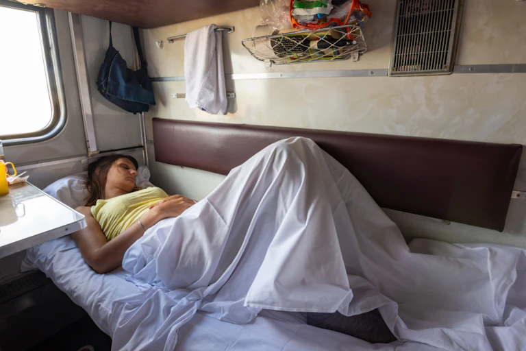 A young woman asleep on a bunk inside a train.