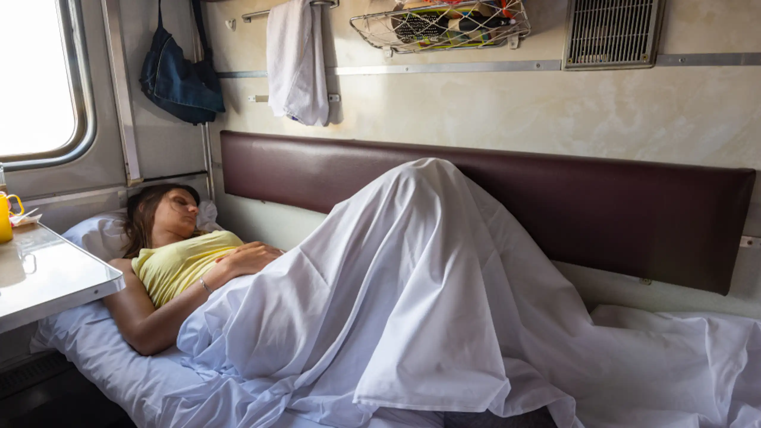 A young woman asleep on a bunk inside a train.