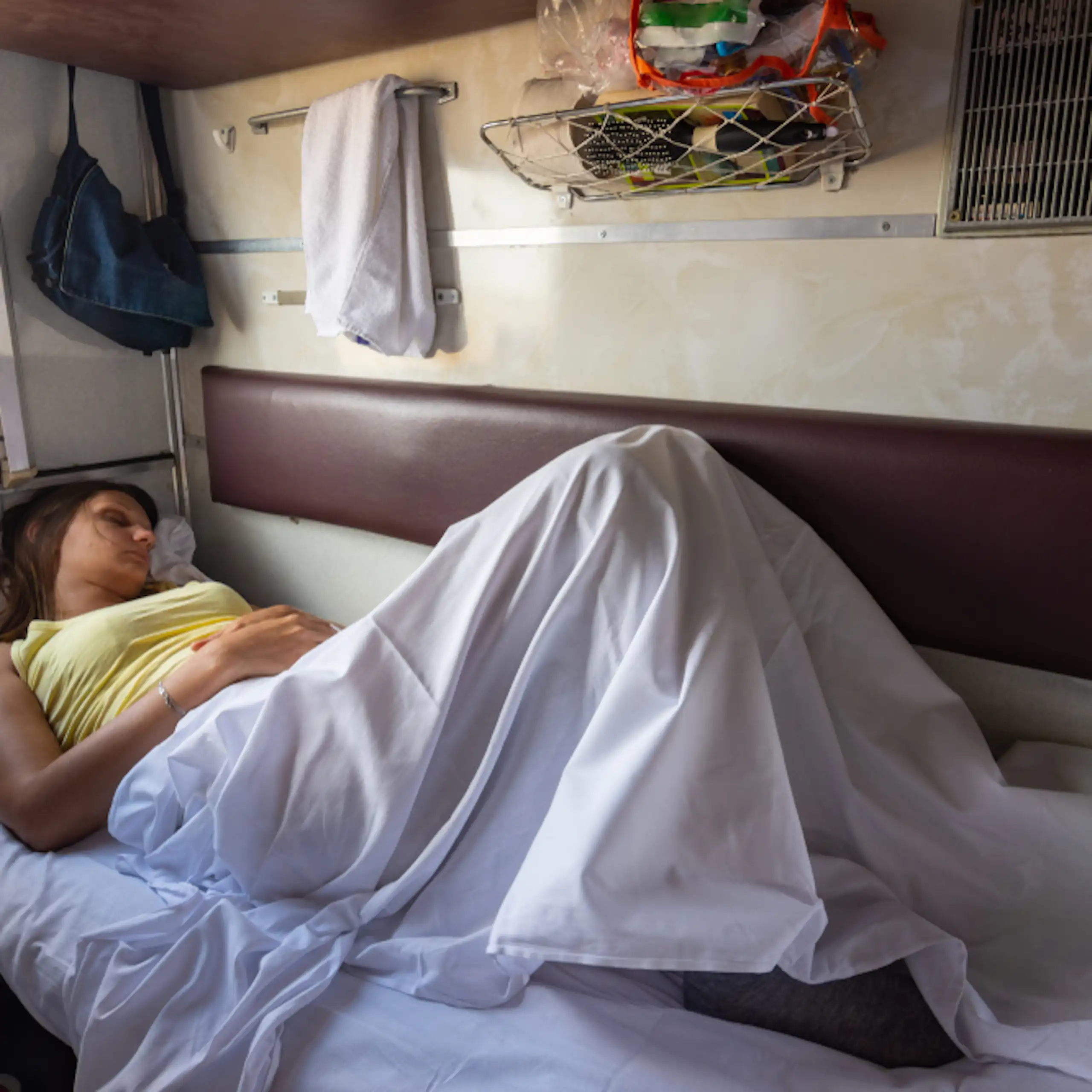 A young woman asleep on a bunk inside a train.