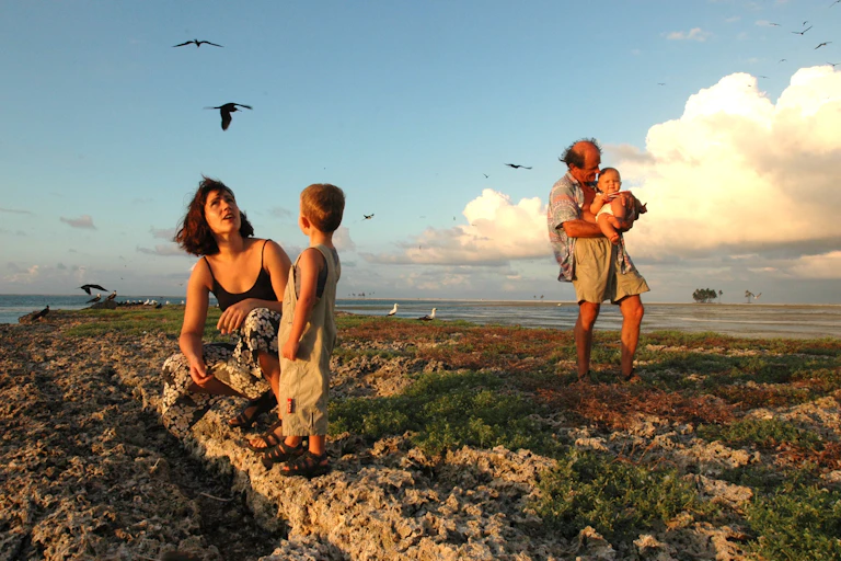 A mom, a dad and two young kids traverse rocky terrain as birds fly over them.