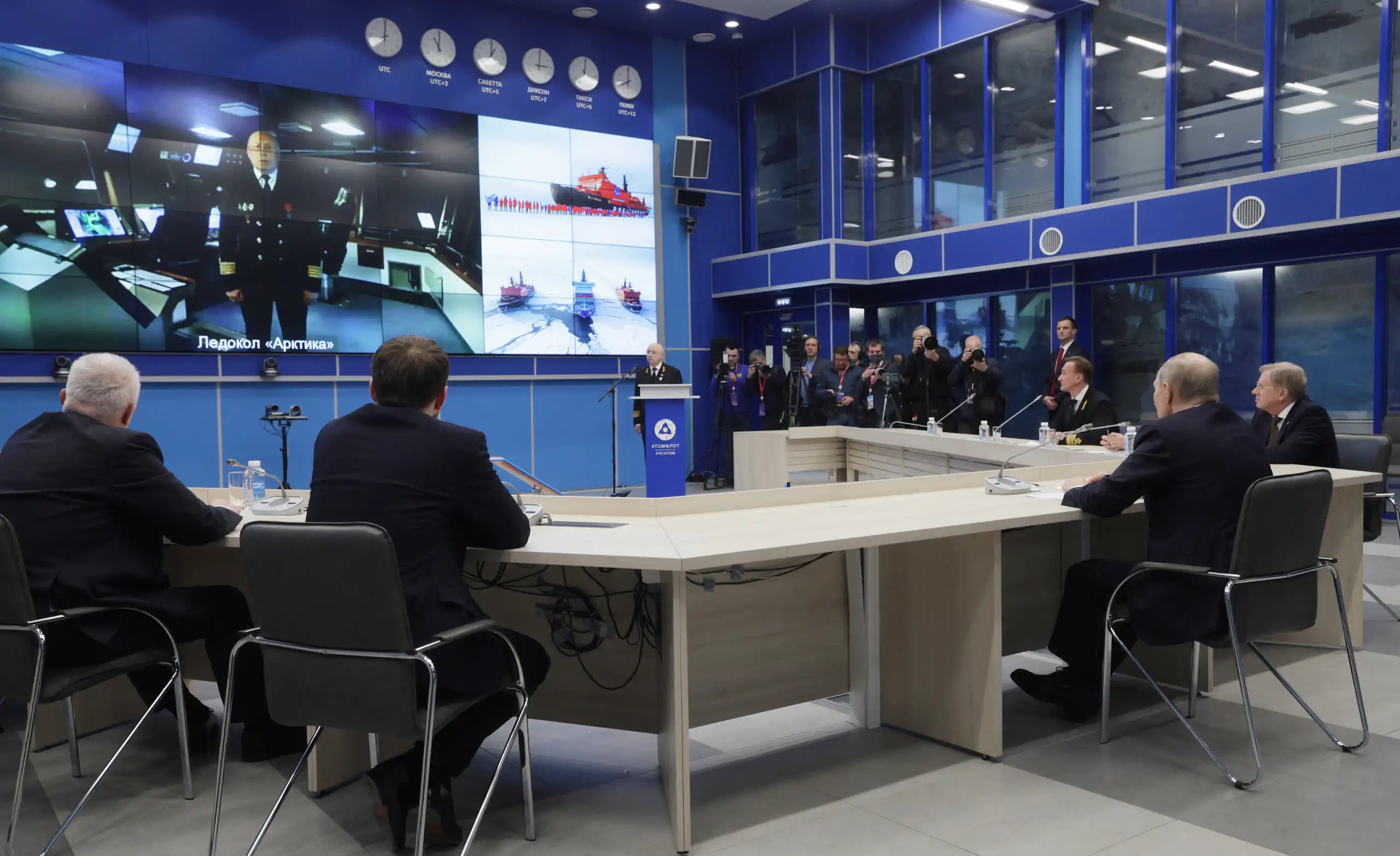 Vue sur la table de la réunion autour de laquelle des officiers et Vladimir Poutine échangent en visioconférence avec un officier.