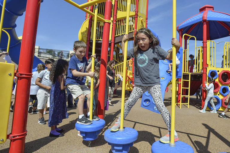 A group of young children are seen playing on bright, colorful playground equipment.