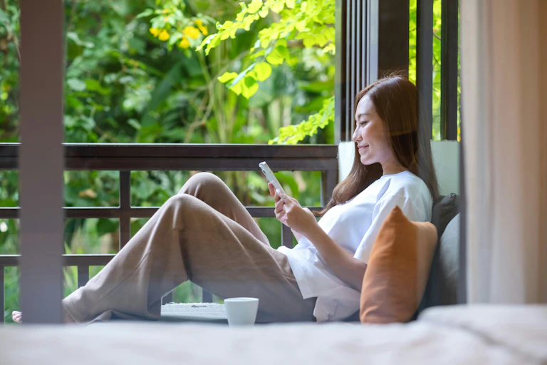 A woman sitting by a window relaxing with her phone)