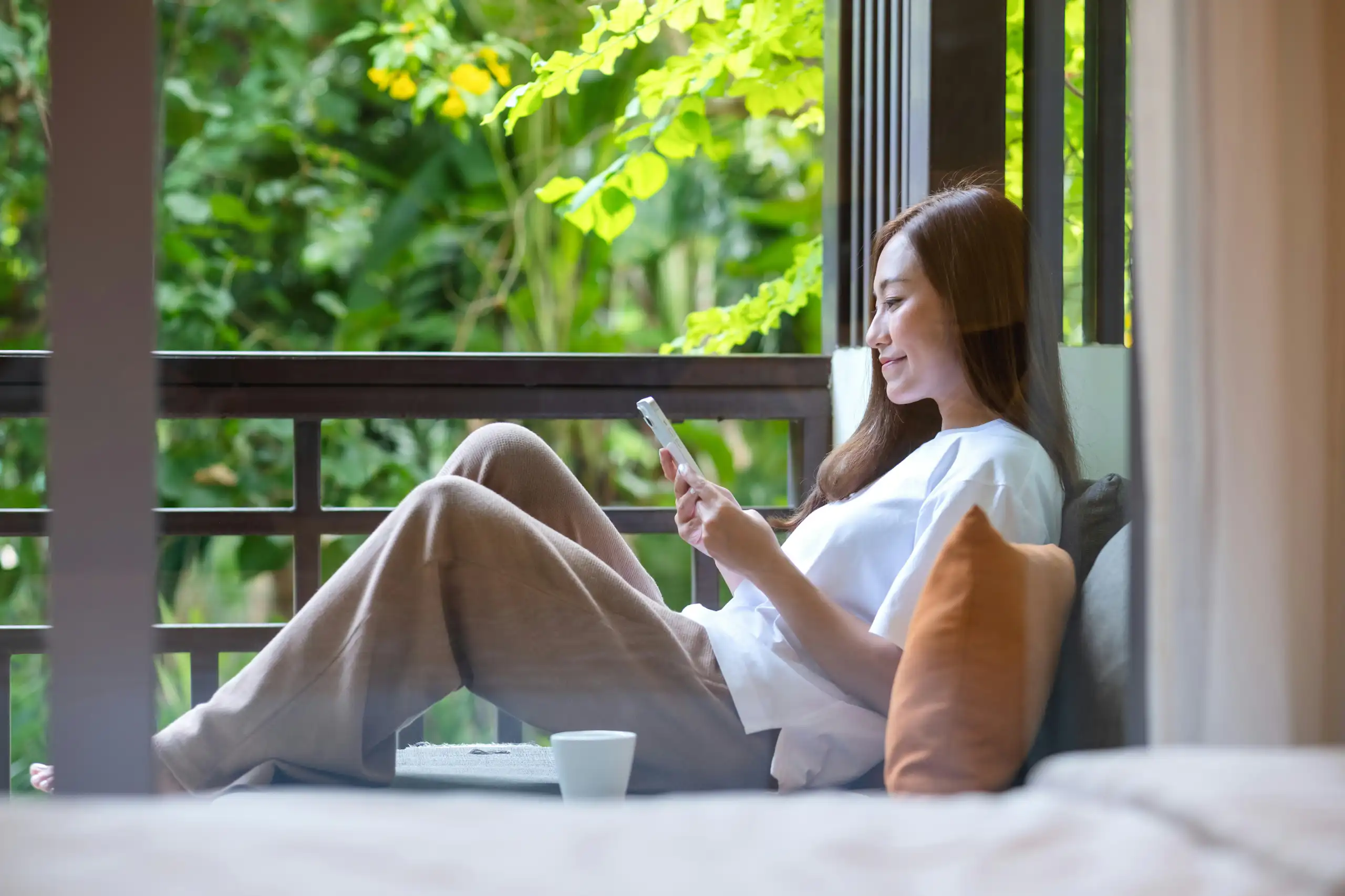 A woman sitting by a window relaxing with her phone)