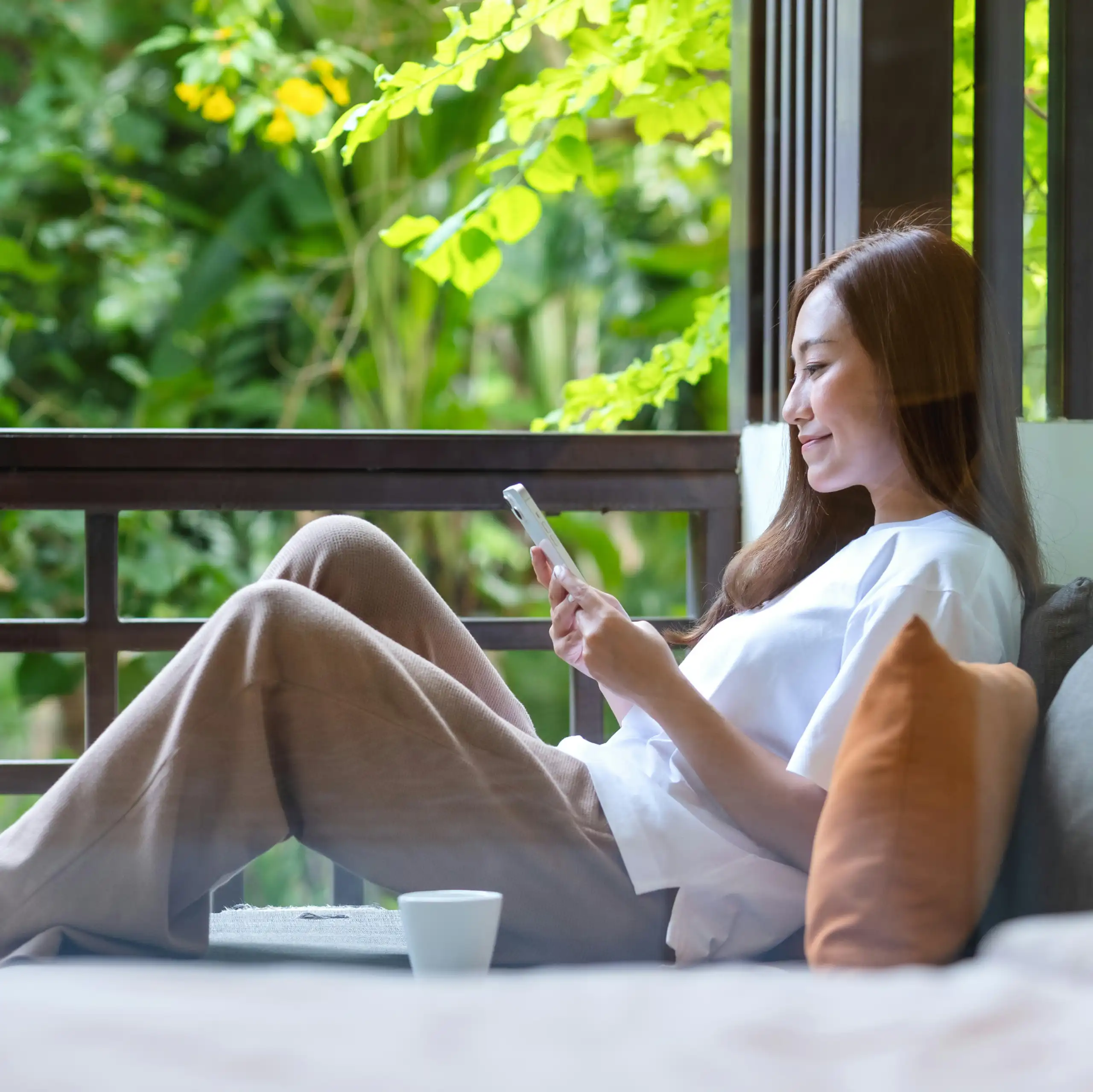 A woman sitting by a window relaxing with her phone)