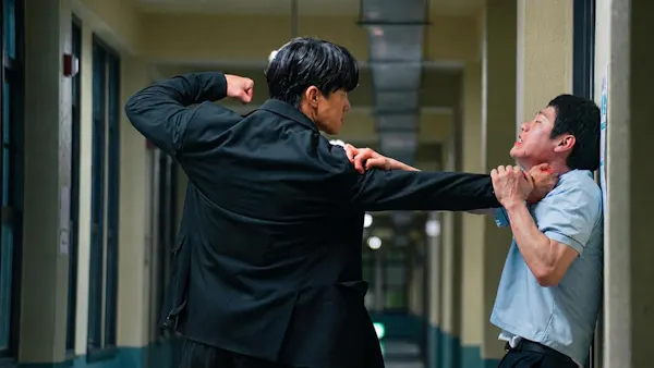 In a hallway, one man has another pinned against the wall as he gets ready to punch him.