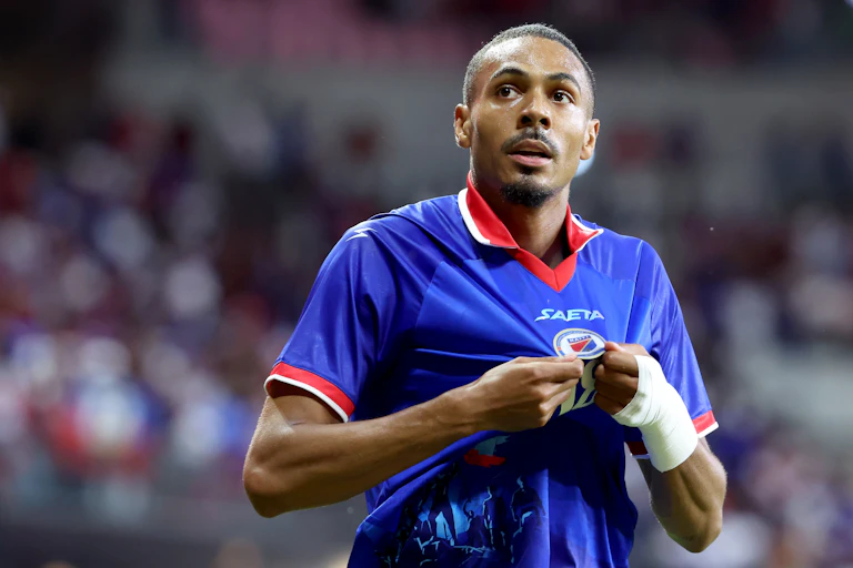 Young Black man tugs on his blue and red soccer jersey during a match.