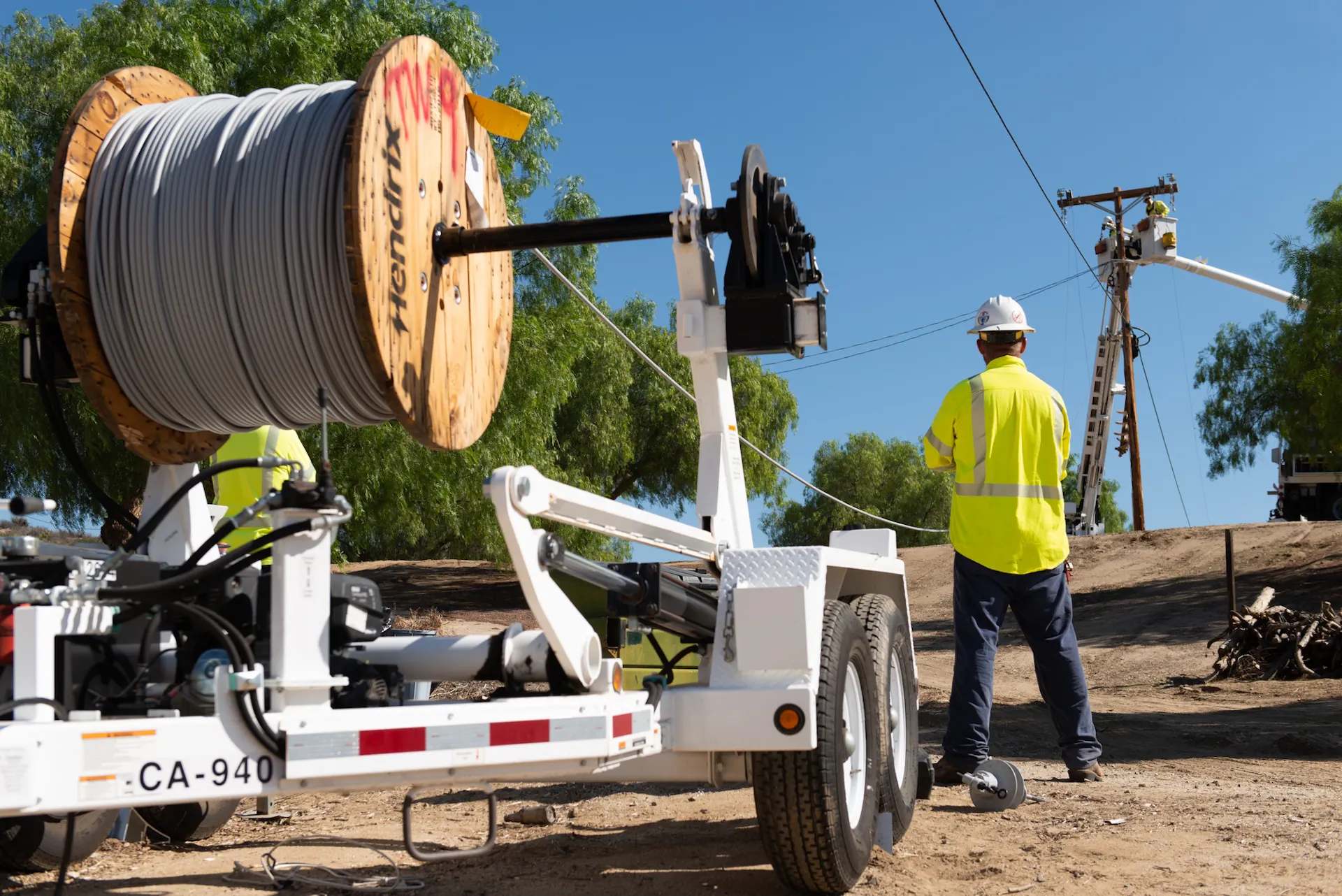 A worker stands by a giant roll of covered conductor line – power lines covered in a plastic.