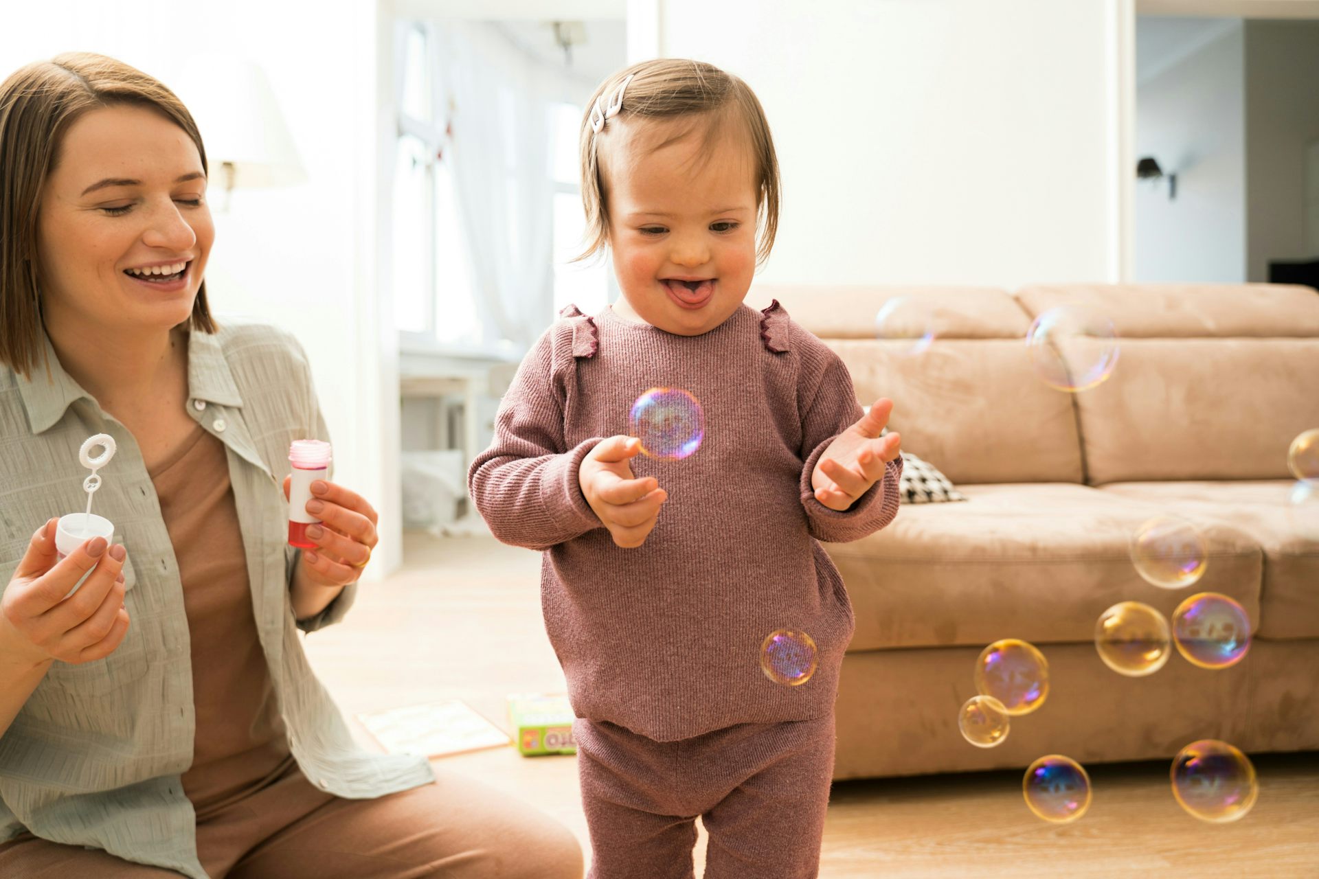 A woman blowing bubbles with her toddler who is smiling.