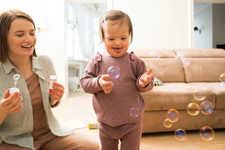 A woman blowing bubbles with her toddler who is smiling.