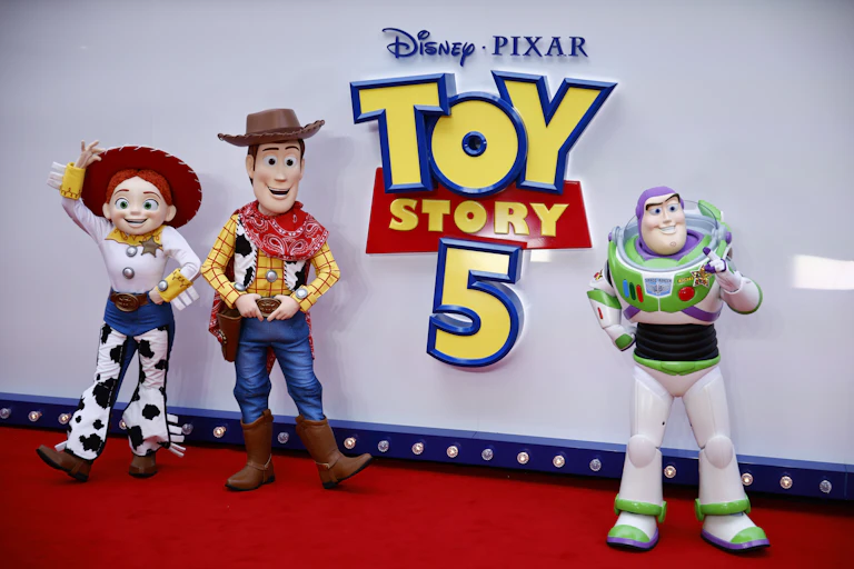 Life size Toy Story characters post in front of a 'Toy Story 5' sign on a red carpet.