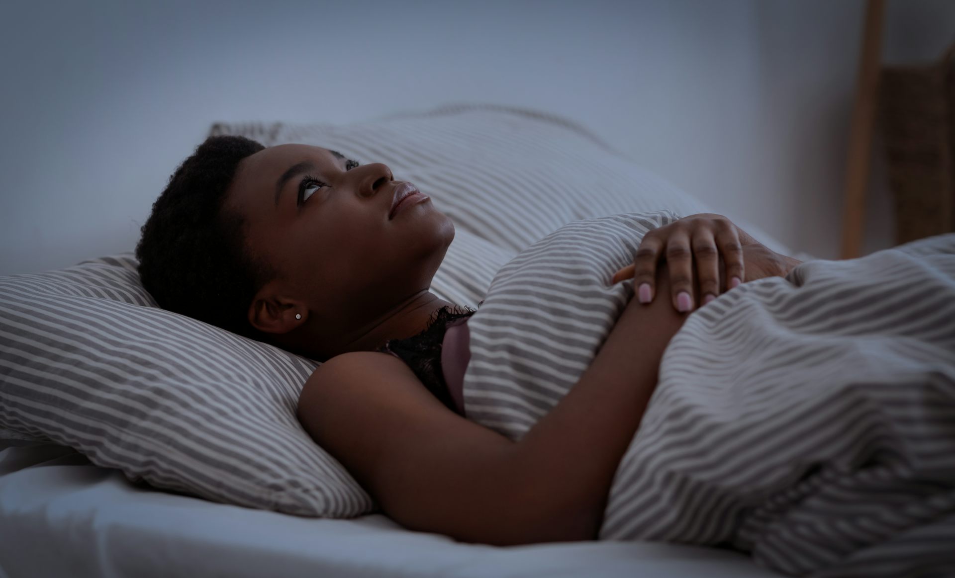 A young woman lies awake in bed at night.