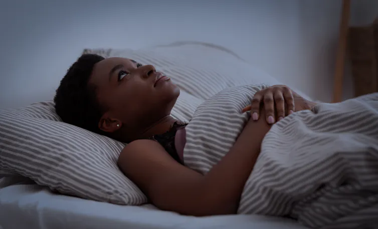 A young woman lies awake in bed at night.