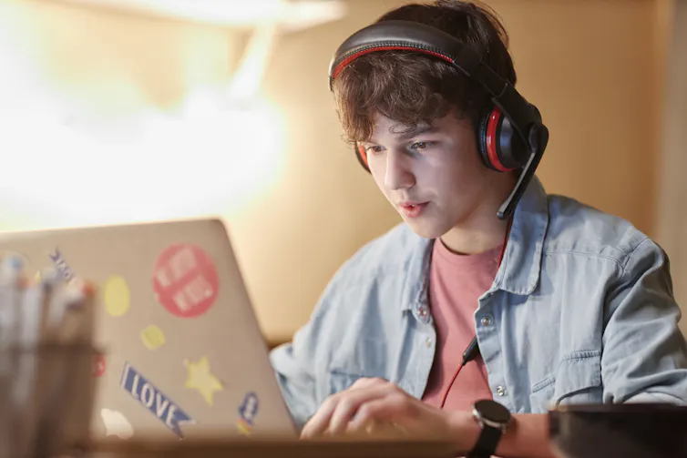 Teen boy wearing a headset and looking at a laptop.