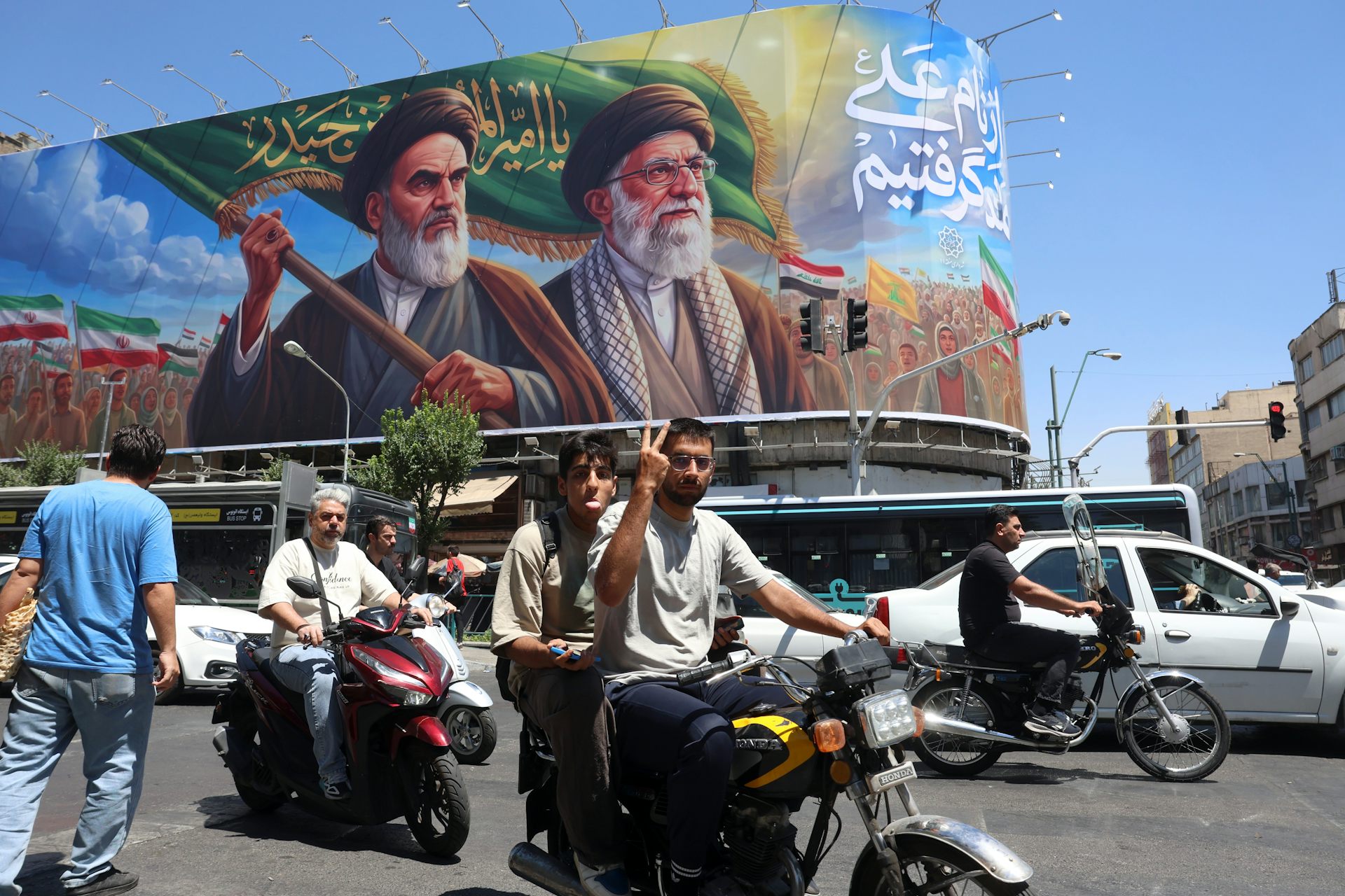 Iranians ride motorcycles in Tehran past a poster of late Iranian supreme leaders Ayatollah Ruhollah Khomeini and Ayatollah Ali Khamenei .