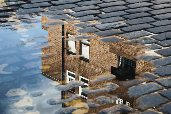 A house reflected in a puddle on cobblestones