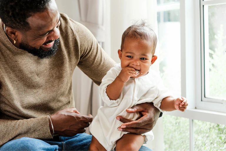 Smiling father holds his baby near a sunny window,