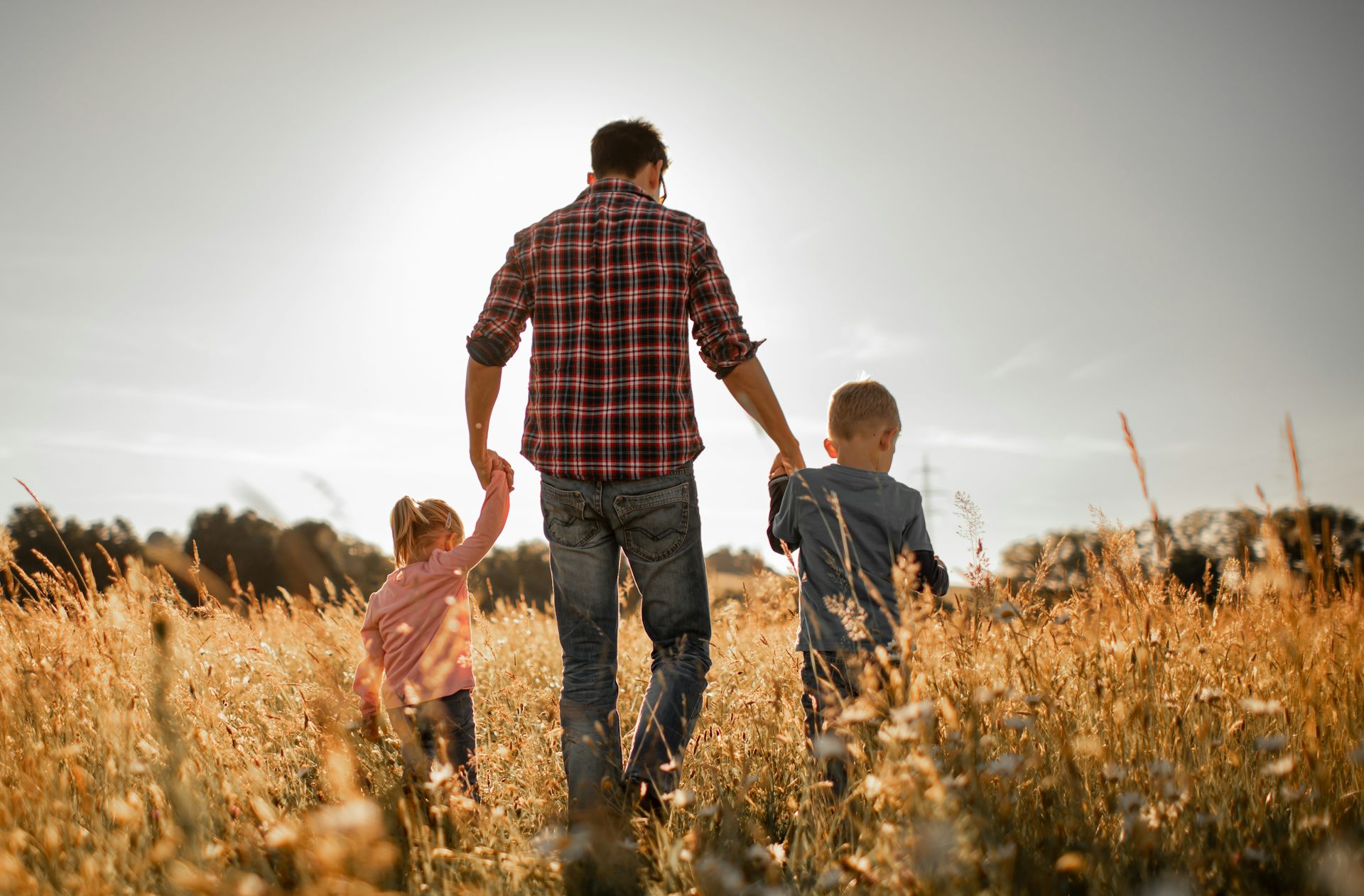 Father walking in nature meadow with his two children.