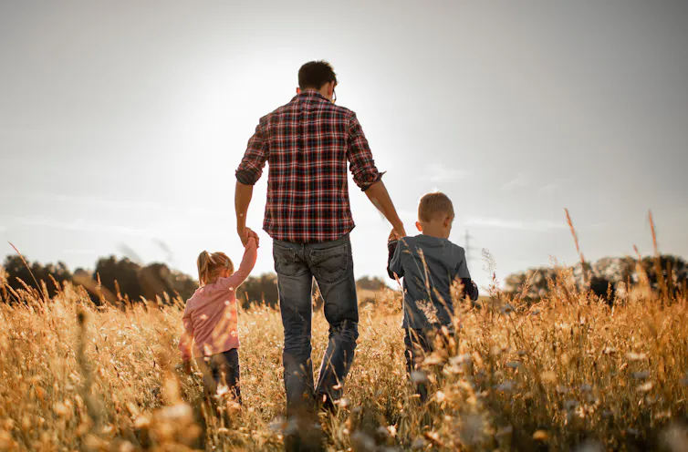 Father walking in nature meadow with his two children.