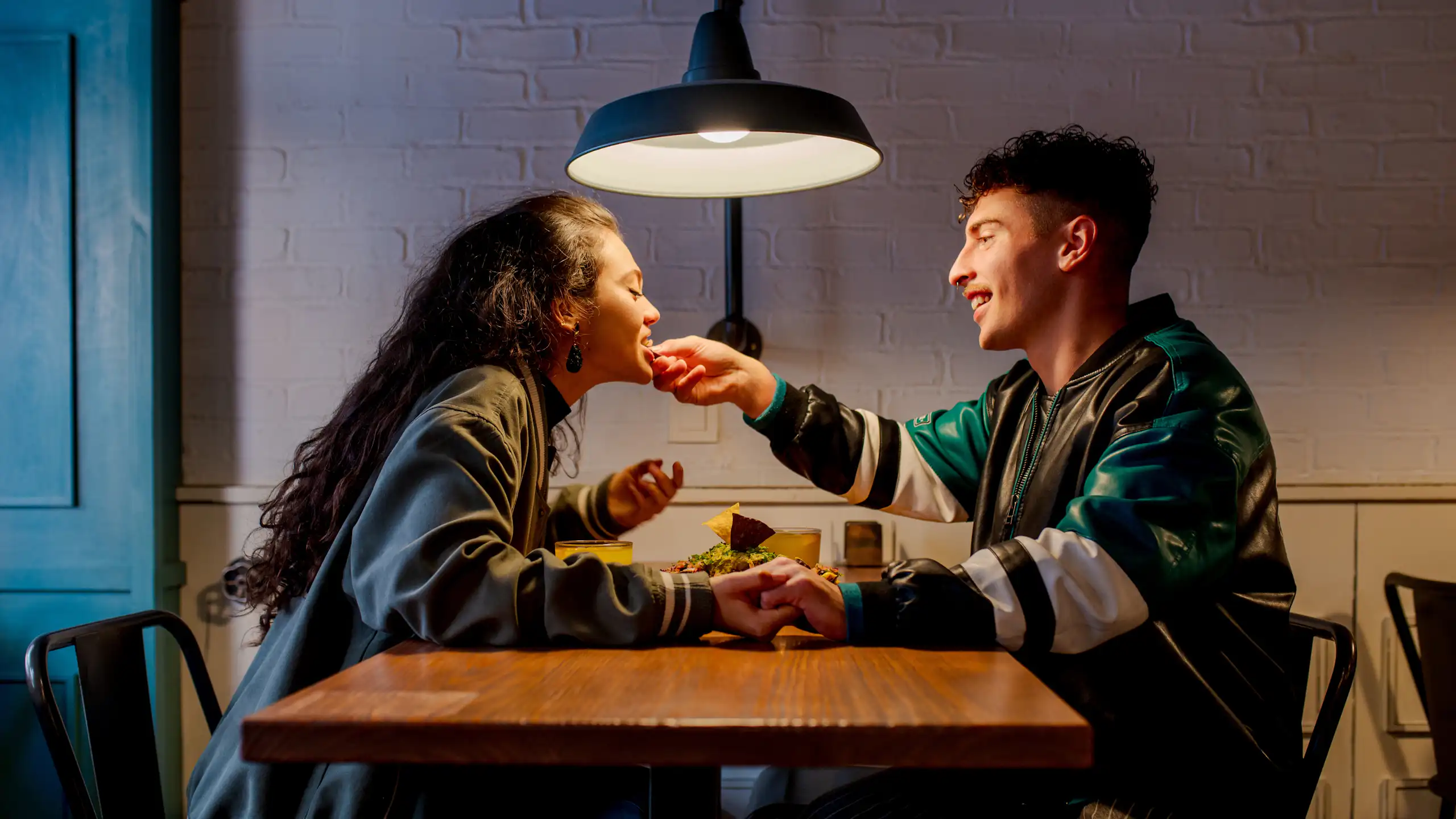 Un jeune couple partageant un repas intime ; un homme se penche au-dessus de la table pour toucher la lèvre inférieure de sa petite amie.